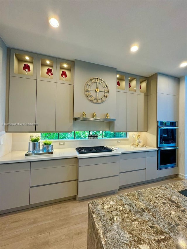 kitchen with gas cooktop, stainless steel double oven, light wood-style flooring, glass insert cabinets, and modern cabinets