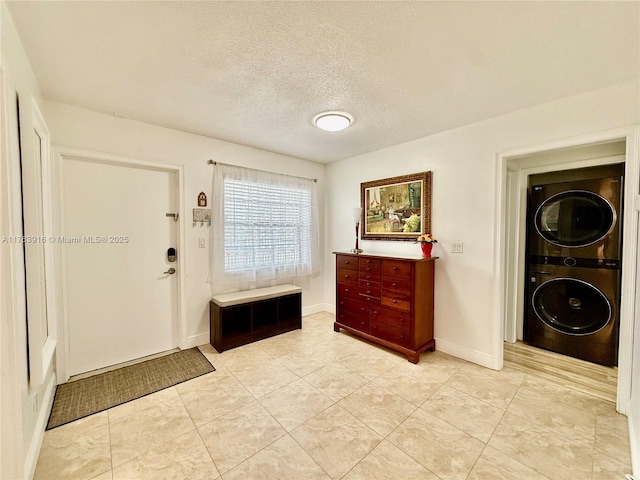 foyer featuring light tile patterned floors, baseboards, a textured ceiling, and stacked washer / dryer