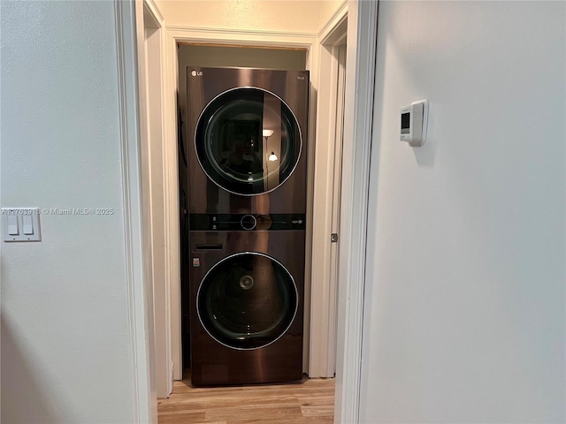 clothes washing area with laundry area, stacked washer and dryer, and wood finished floors