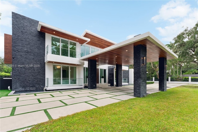 back of house featuring stone siding, stucco siding, a lawn, and a balcony