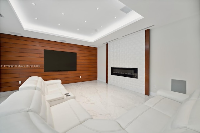 living room featuring a tray ceiling, a fireplace, wood walls, an accent wall, and marble finish floor