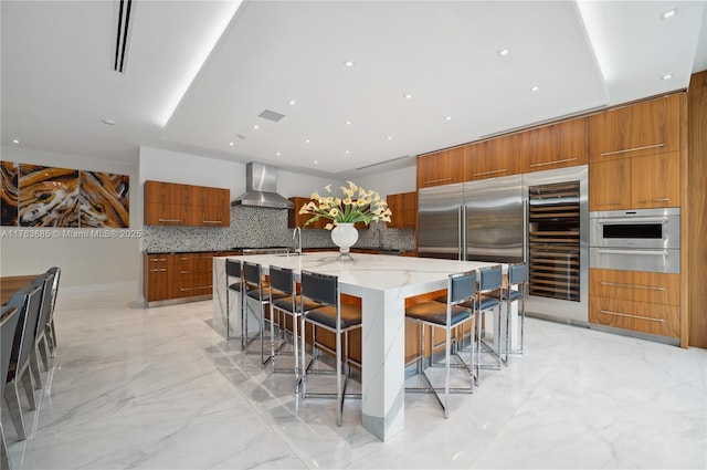 kitchen with wall chimney range hood, appliances with stainless steel finishes, brown cabinetry, marble finish floor, and modern cabinets