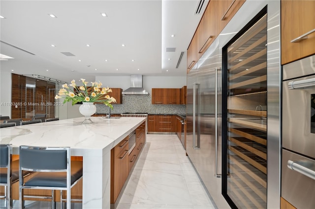 kitchen featuring brown cabinets, modern cabinets, a sink, light stone counters, and wall chimney exhaust hood