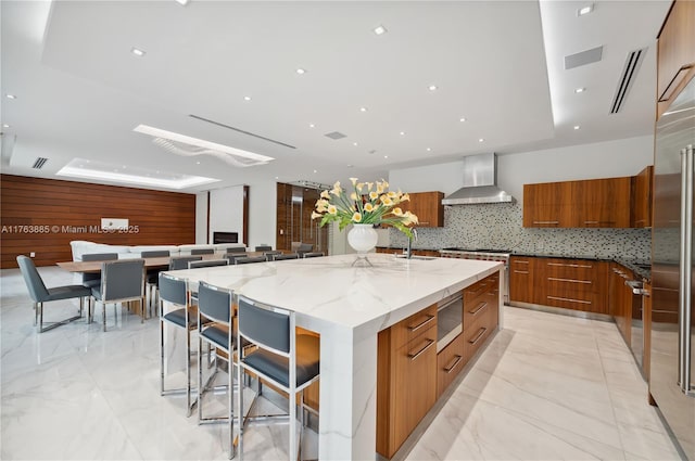 kitchen with brown cabinets, modern cabinets, marble finish floor, and wall chimney range hood