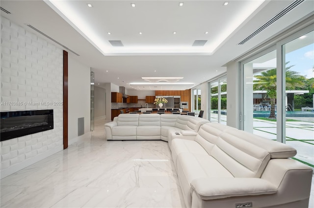 living room featuring a tray ceiling, a fireplace, and marble finish floor