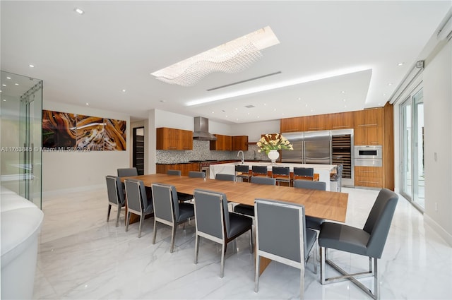 kitchen featuring brown cabinets, decorative backsplash, built in refrigerator, wall chimney exhaust hood, and marble finish floor