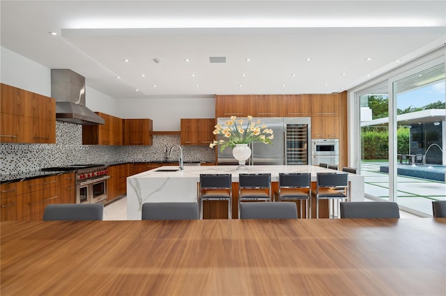 kitchen featuring brown cabinets, modern cabinets, wall chimney exhaust hood, and stainless steel appliances