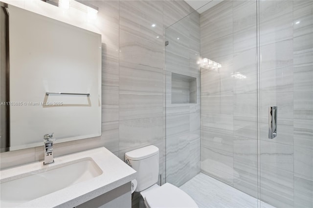 full bathroom with vanity, a shower stall, toilet, and tile walls