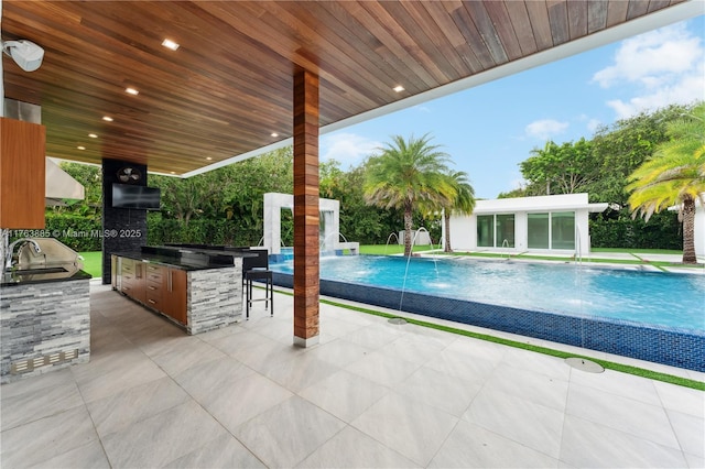 pool featuring outdoor wet bar, an outbuilding, an outdoor kitchen, a patio, and a sink