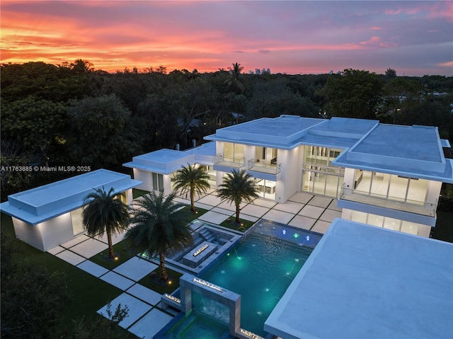 pool at dusk with a patio area and a pool with connected hot tub