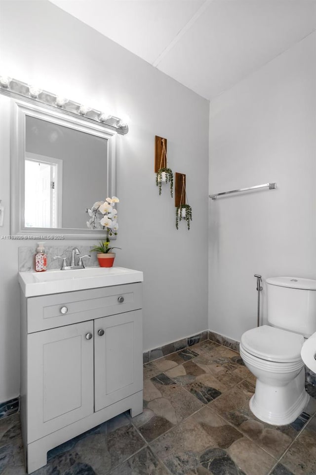 half bathroom featuring vanity, toilet, baseboards, and stone tile flooring