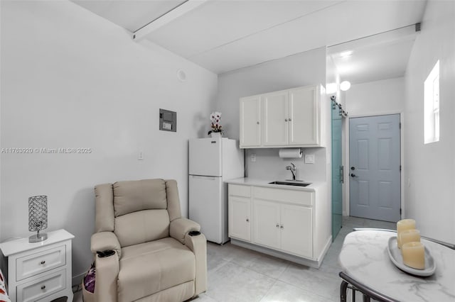 kitchen featuring freestanding refrigerator, a sink, light countertops, white cabinets, and open floor plan