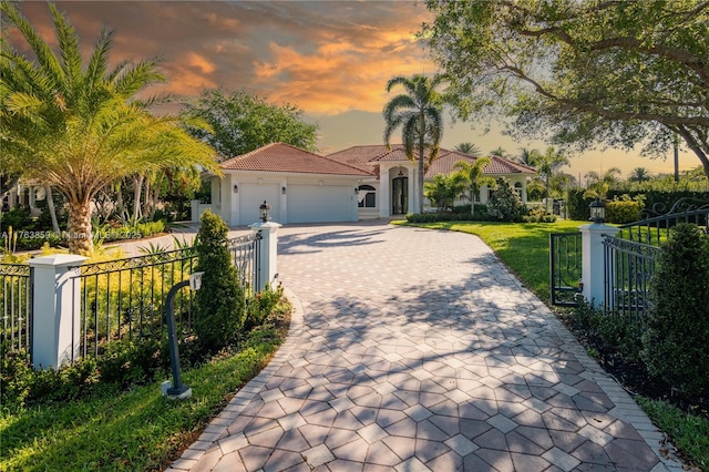 mediterranean / spanish-style home featuring a tiled roof, fence private yard, stucco siding, decorative driveway, and a garage