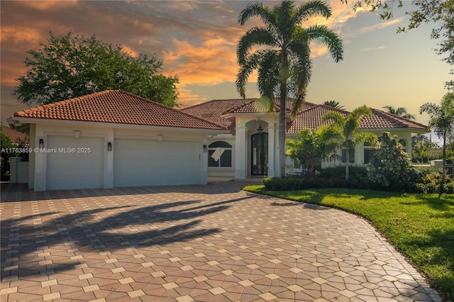 mediterranean / spanish-style house featuring an attached garage, a tile roof, and decorative driveway