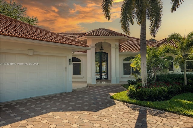 view of front facade with stucco siding, a tiled roof, an attached garage, and driveway