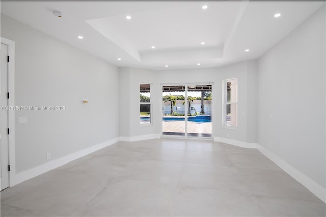 unfurnished room with recessed lighting, a tray ceiling, and baseboards