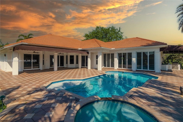 pool at dusk with a patio, area for grilling, ceiling fan, and a pool with connected hot tub