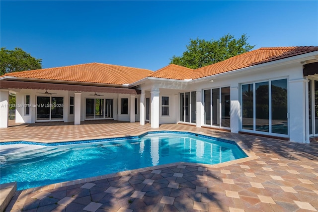 back of house with stucco siding, a tiled roof, an outdoor pool, ceiling fan, and a patio area