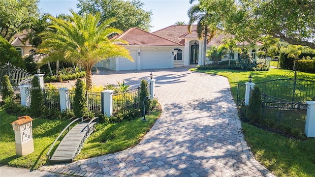 mediterranean / spanish home featuring a front yard, an attached garage, a fenced front yard, a tiled roof, and decorative driveway