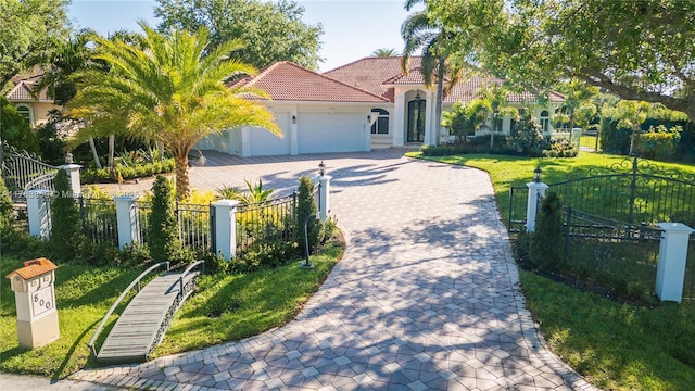 mediterranean / spanish house featuring a front lawn, a fenced front yard, decorative driveway, an attached garage, and a tiled roof