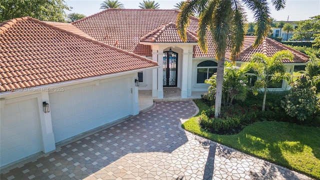 mediterranean / spanish-style home featuring a tiled roof, an attached garage, driveway, and stucco siding