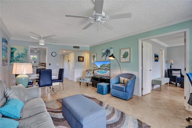 living area featuring crown molding, ceiling fan, light tile patterned floors, wainscoting, and a textured ceiling