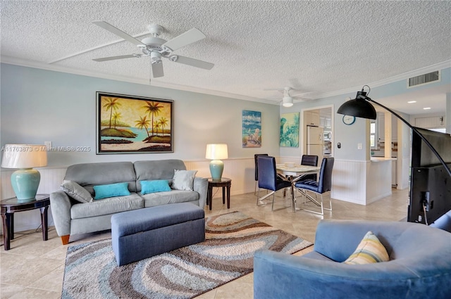 living area featuring visible vents, crown molding, ceiling fan, and a wainscoted wall