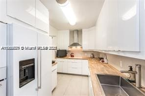 kitchen featuring a sink, wall chimney exhaust hood, white cabinets, light countertops, and light tile patterned floors