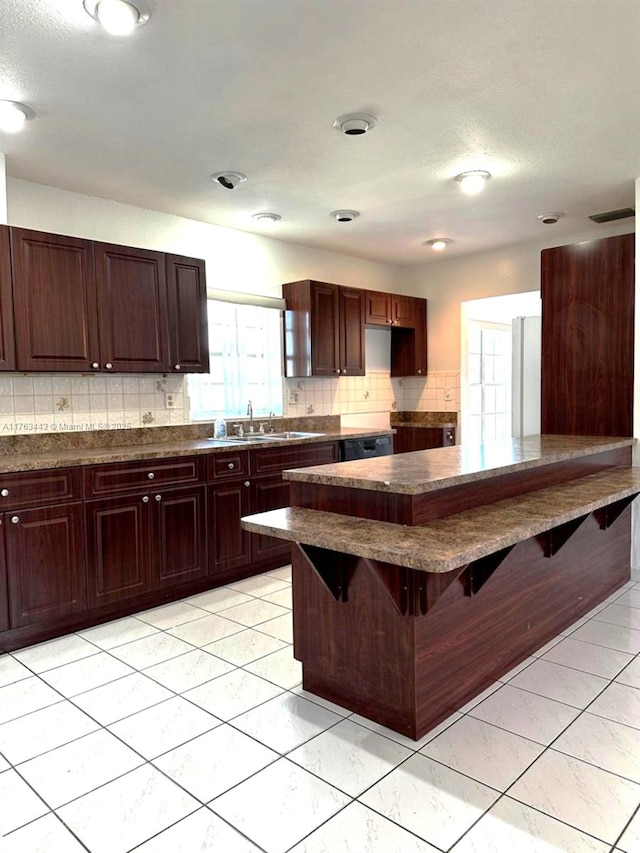 kitchen with a sink, tasteful backsplash, dark countertops, a breakfast bar area, and dark brown cabinets