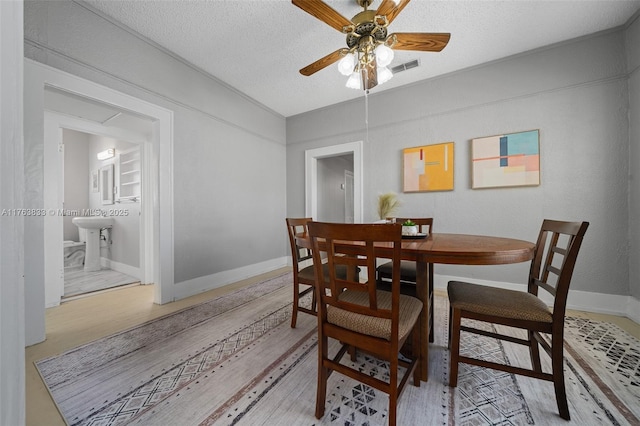 dining area with light wood-type flooring, visible vents, a textured ceiling, baseboards, and ceiling fan