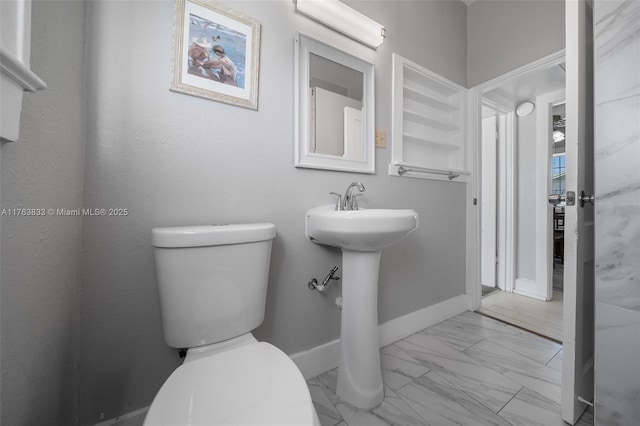 bathroom with marble finish floor, toilet, and baseboards