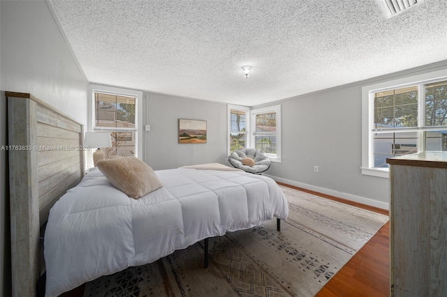 bedroom featuring visible vents, baseboards, a textured ceiling, and wood finished floors