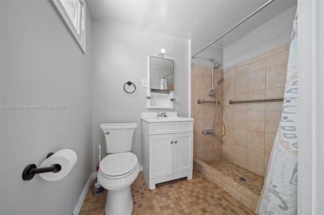 bathroom with toilet, tiled shower, vanity, and baseboards