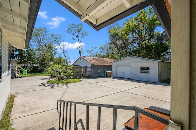 view of patio featuring a detached garage, an outdoor structure, concrete driveway, and fence