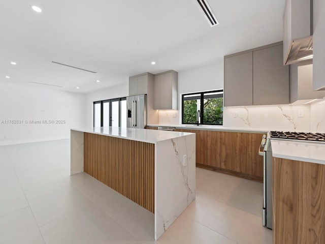 kitchen featuring modern cabinets, gray cabinetry, backsplash, a kitchen island, and appliances with stainless steel finishes