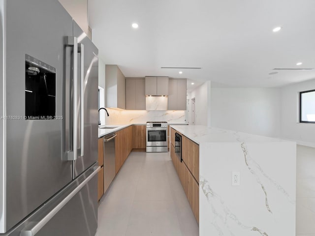 kitchen with modern cabinets, light stone counters, backsplash, a spacious island, and appliances with stainless steel finishes