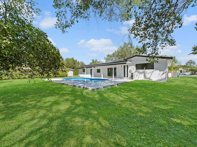 back of house with a patio area, a lawn, an outdoor pool, and stucco siding