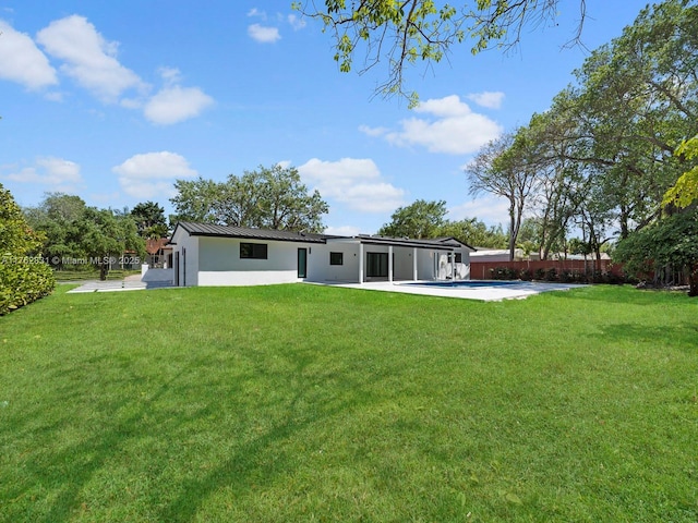 rear view of house featuring stucco siding, a lawn, fence, metal roof, and a patio area