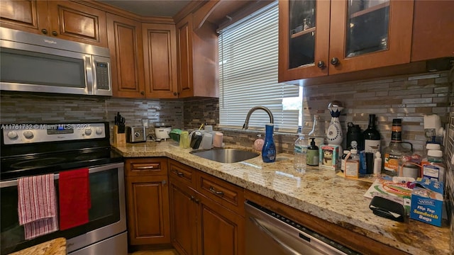 kitchen featuring backsplash, light stone counters, brown cabinetry, stainless steel appliances, and a sink