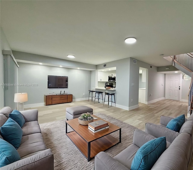 living area featuring baseboards, stairs, and light wood finished floors