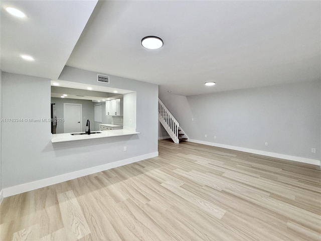 unfurnished living room featuring visible vents, light wood-style flooring, a sink, stairway, and baseboards