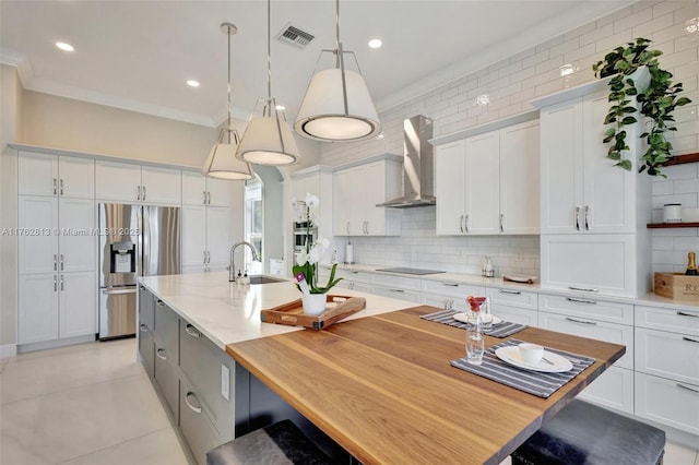 kitchen with a sink, appliances with stainless steel finishes, white cabinetry, wall chimney range hood, and backsplash