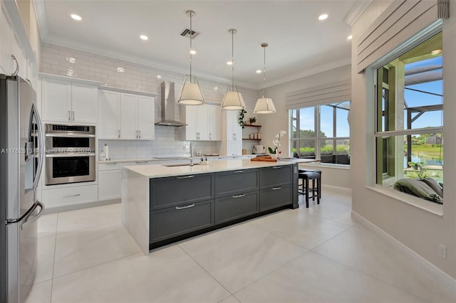 kitchen featuring visible vents, a sink, tasteful backsplash, appliances with stainless steel finishes, and wall chimney range hood