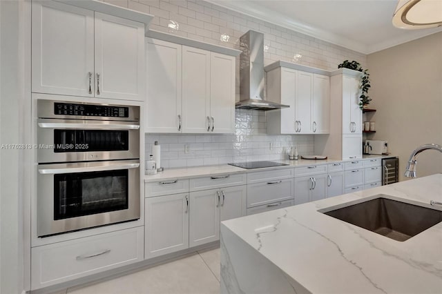 kitchen featuring stainless steel double oven, a sink, ornamental molding, wall chimney exhaust hood, and backsplash