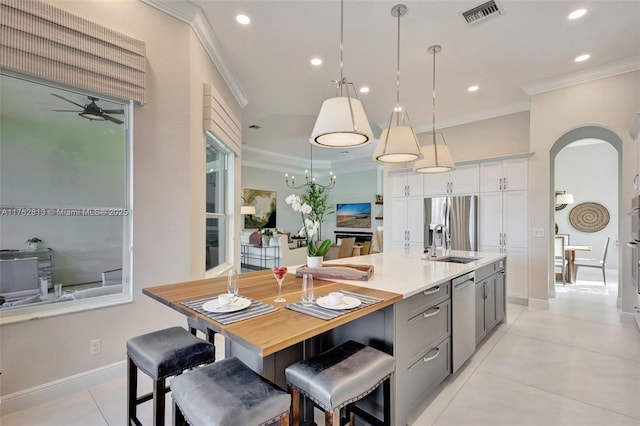 kitchen featuring visible vents, ornamental molding, ceiling fan with notable chandelier, stainless steel appliances, and a sink