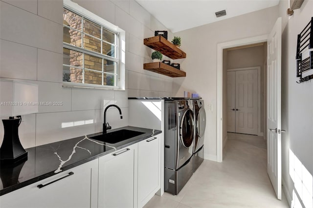 laundry area featuring visible vents, a sink, washing machine and dryer, cabinet space, and baseboards