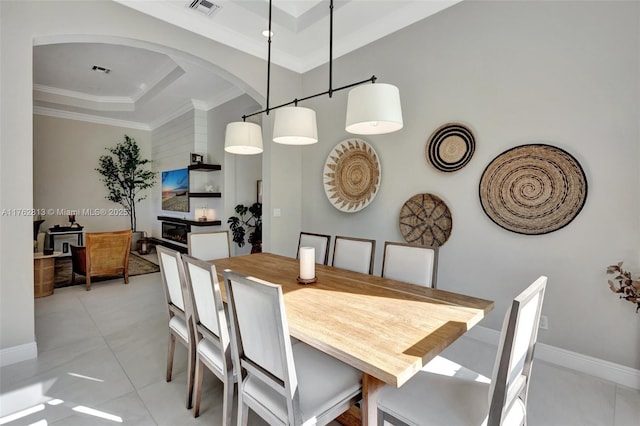 dining room featuring crown molding, baseboards, a tray ceiling, light tile patterned flooring, and arched walkways