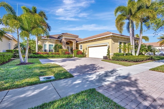 mediterranean / spanish home with a tiled roof, an attached garage, decorative driveway, and a front lawn