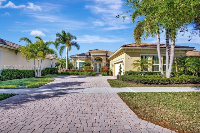 mediterranean / spanish home with a tile roof, a front yard, stucco siding, decorative driveway, and a garage