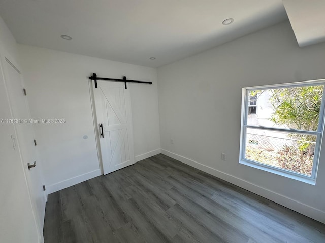 unfurnished bedroom with recessed lighting, baseboards, dark wood-type flooring, and a barn door